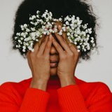 woman in red top covering face with white flowers