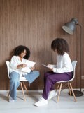 two light skinned women sitting down going though work