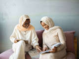 two muslim women in cream reading and smiling