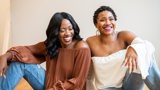 two black women sitting with arms on knees laughing