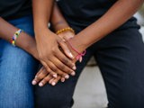 two black people holding four hands with African beads