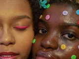 two black women with colourful makeup and buttons on faces