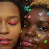 two black women with colourful makeup and buttons on faces