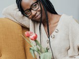 black woman in glasses on yellow sofa holding flowers