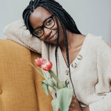 black woman in glasses on yellow sofa holding flowers