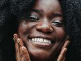 black woman smiling with afro hair with hands on face