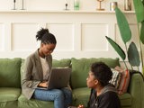 black woman with laptop on soft and black girl sitting on the floor